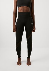 Leggings neri a vita alta con pannelli trasparenti; progettati per flessibilità e comfort; presentano un dettaglio del logo sull'anca.