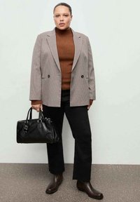 Geruit blazer in lichte en donkere tinten, bruine geribbelde coltrui, zwarte broek en zwarte leren handtas. Bruine enkellaarsjes maken de outfit compleet.