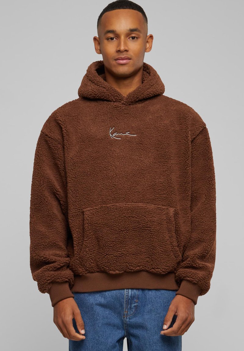 Rudas pūkų džemperis su tekstūruotu paviršiumi, priekinė kišenė, raukšlėti rankogaliai ir šnervelė ant kapučino; turi baltą siuvinėtą logotipą.