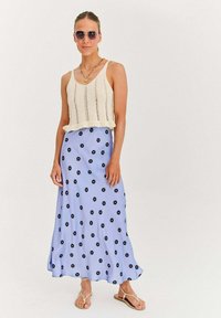 Pletený krémový top bez rukávov je skombinovaný s svetlomodrou maxi sukňou s čiernymi kvetinovými vzormi. Model má na sebe slnečné okuliare a ploché sandále.