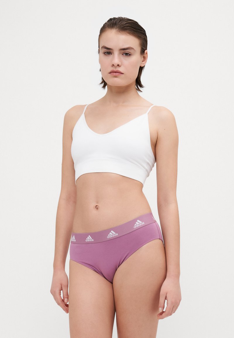 Lehký bílý bralet s tenkými ramínky, který je spárován s růžovými bikinovými kalhotkami se širokým páskem s logem a hladkým, přiléhavým designem.