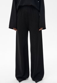 Czarne spodnie o szerokich nogawkach i luźnym kroju, wykonane z miękkiej, teksturowanej tkaniny. Posiadają elastyczny pas i prążkowane ściągacze przy kostkach.