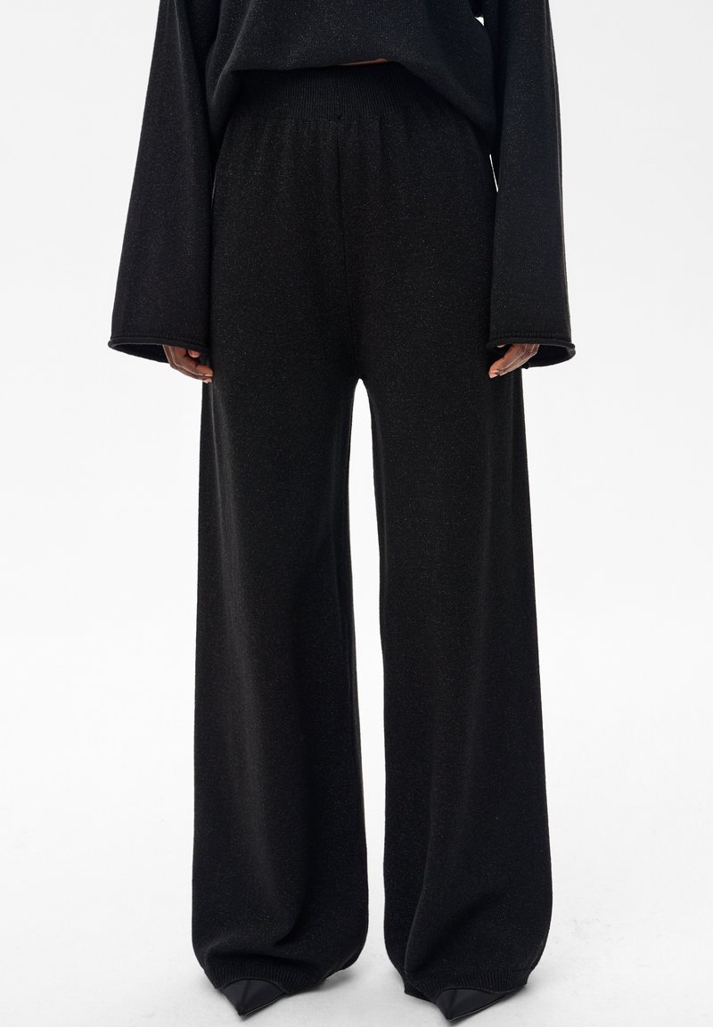 Czarne spodnie o szerokich nogawkach i luźnym kroju, wykonane z miękkiej, teksturowanej tkaniny. Posiadają elastyczny pas i prążkowane ściągacze przy kostkach.