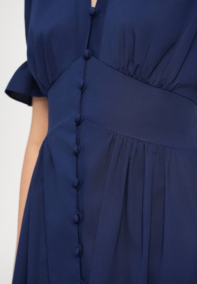 Σκούρο μπλε φόρεμα με κουμπιά μπροστά, κοντά μανίκια και πλισέ ύφασμα στη φούστα, κατασκευασμένο από ελαφρύ υλικό.