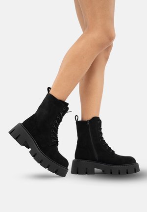 Black suede ankle boots with front laces and side zipper, featuring chunky black platform soles with cut-out designs.