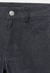 Temno modri džins hlače v bližnjem posnetku prikazujejo pas, gumb, zanko za pas in detajle šivanja sprednjega žepa.