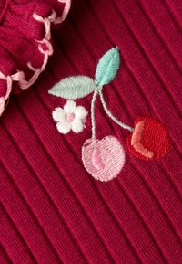 Burgunderroter gerippter Stoff mit einer Rüsche; bestickte Kirschen in Rot und Pink, mit einer weißen Blume und hellgrünen Blättern.