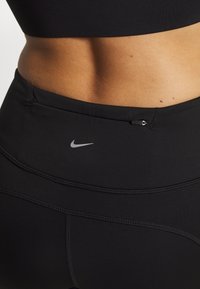 Czarne sportowe legginsy z elastycznego materiału z wysokim stanem, wyposażone w małe logo Nike oraz dodatkową kieszeń zabezpieczającą na pasku.