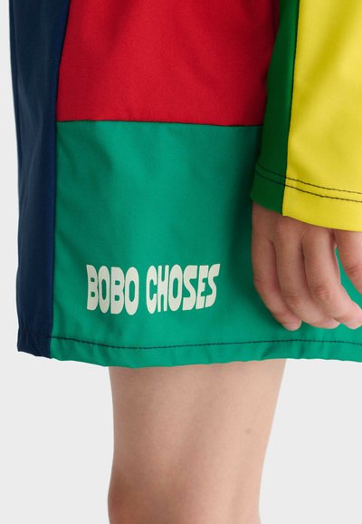 Lower body wearing colorful shorts with red, green, navy, and yellow panels, showing "BOBO CHOSES" text on the green panel.