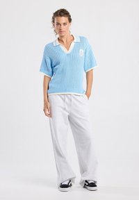 Light blue short-sleeve mesh polo sweater with white accents, paired with grey sweatpants. Features a V-neck and front pocket detail.