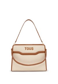 Bolso de lona con detalles y correa para el hombro en cuero marrón claro. Presenta el logo "TOUS" en relieve. Forma rectangular, textura lisa y detalles curvos.