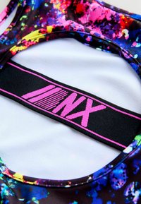 Kolorowy stanik sportowy z jaskrawym wzorem rozbryzgów na czarnym tle, z różowym logo i kontrastującym białym wnętrzem.