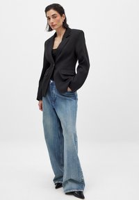 Svart jacka med snedskuren krage och två framfickor, kombinerad med vida ljusblå jeans och svarta pumps med spetsig tå.