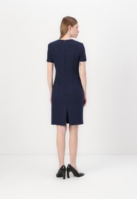 Mornarsko modra oprijeta obleka s kratkimi rokavi, zadrgo na hrbtu in razporkom na robu. Gladek material z oblikovano detajlno zasnovo na hrbtu.