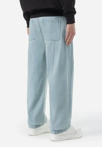 Lichtblauwe denim broek met een recht gesneden ontwerp, twee achterzakken en subtiele stikdetails, gecombineerd met witte sneakers.