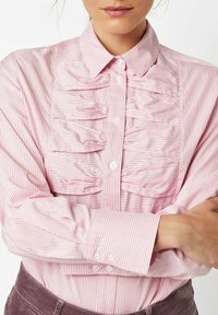 Pink button-up shirt featuring vertical white stripes, textured ruffles down the front, and double button cuffs. Smooth fabric finish.