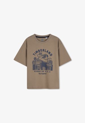 Bruine Timberland T-shirt met een marineblauwe afbeelding van een laars en winkelvoorzijde, inclusief tekst "Since 1973" en "New England U.S.A."