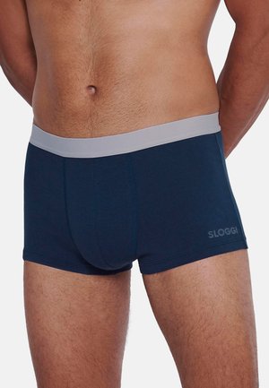 Männlicher Oberkörper, bekleidet mit marineblauen Boxershorts mit einem hellgrauen Bund, auf dem linken Oberschenkel befindet sich der Markenname "Sloggi".