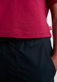 Bordeauxfarbene Baumwoll-T-Shirt mit geradem Saum, kombiniert mit schwarzen Hosen mit elastischem Bund und verstellbarem Kordelzug.
