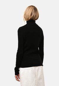 Mustapaitapusero, jossa on pitkät hihat, ribattu kaula-aukko ja hihansuut, slim fit -malli ja pehmeä rakenne, yhdistettynä vaaleaan hameeseen.