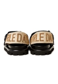 Sandalias de plataforma negras con correas de tela que presentan un texto dorado en relieve. El texto está sobre un fondo beige, con un acabado texturizado y hebilla ajustable.