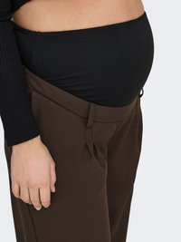 Brown trousers with a loose fit, featuring side pockets and a high waistband. Black undershirt visible at the midsection. Smooth texture.
