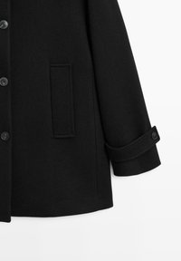 Cappotto di lana nero con una texture liscia, chiusure con bottoni e una tasca laterale singola. Le maniche presentano polsini con bottoni per una regolazione personalizzata.