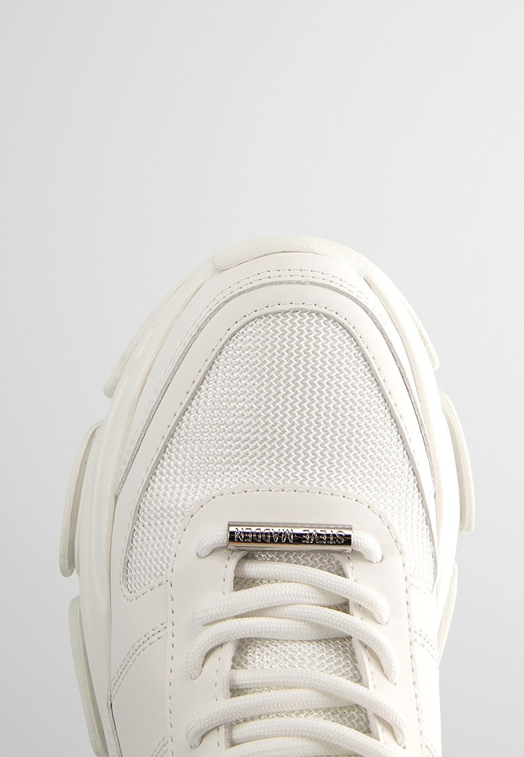Zapatilla blanca con parte superior de malla, cuello acolchado y cordones planos. Presenta un acento de logo metálico en el lateral. Suela texturizada para mayor agarre.