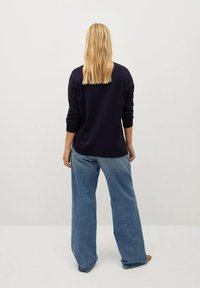 Suéter texturizado azul marino de corte relajado y mangas largas, combinado con pantalones de mezclilla de pierna ancha en azul claro. El modelo es visto desde la parte de atrás.