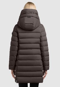 Brązowa puchowa kurtka z wysokim kołnierzem i kapturem, z poziomymi przeszyciami i metką z tyłu, sięgająca do połowy uda.