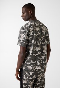 Maglietta mimetica grigia realizzata in tessuto dalla texture morbida. Presenta un motivo distintivo di tonalità chiare e scure e un classico design con collo rotondo.