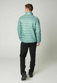 Svijetloplavi pufferjakna s visokim ovratnikom, horizontalnim šavovima i glatkom teksturom, nosi se s crnim hlačama i cipelama, prikazano s leđa.