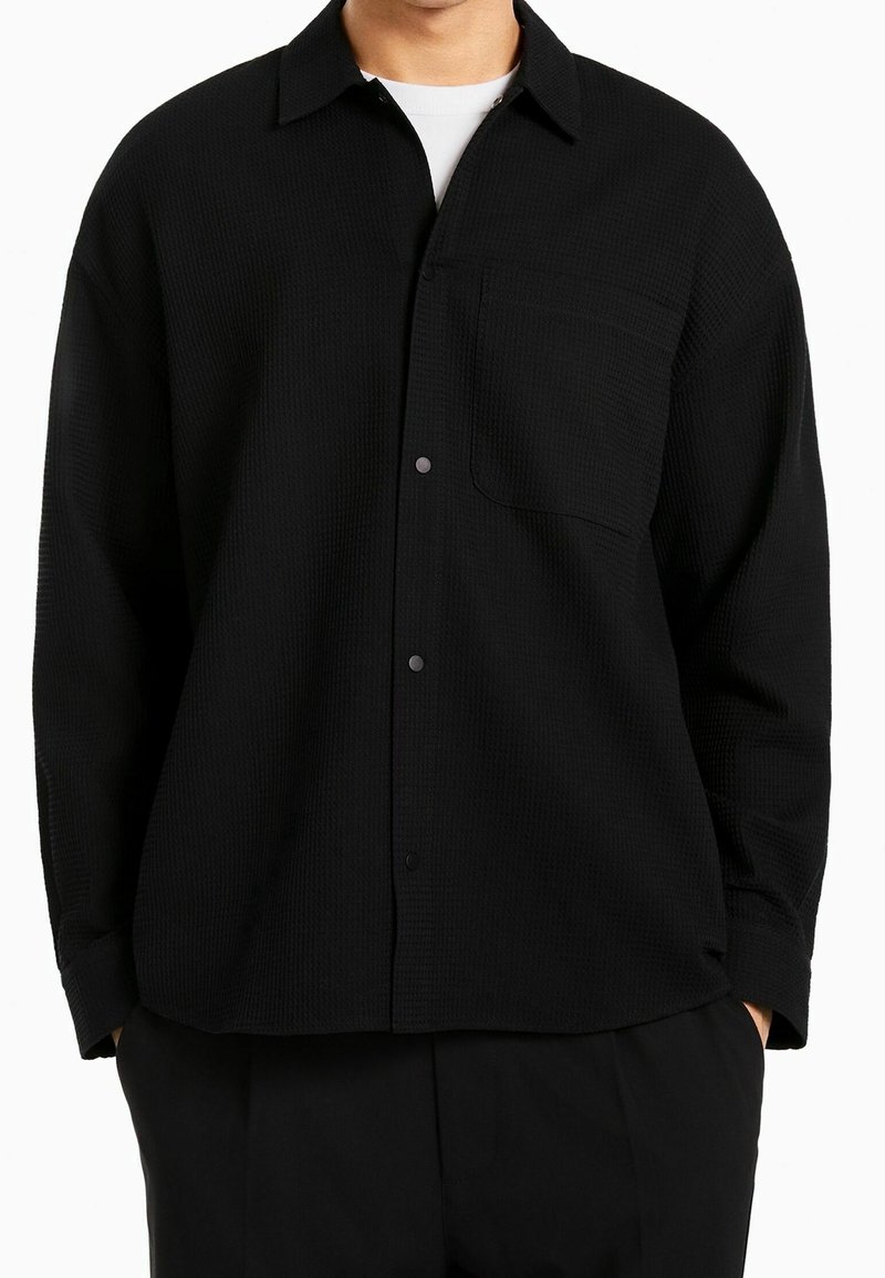 Svart skjorta med knappar i strukturerad tyg, med klassisk krage, en bröstficka och långa ärmar.