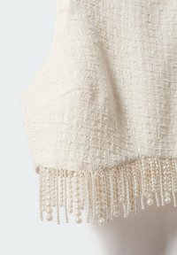 Tissu crème texturé avec un motif en nid d'abeille, présentant une frange de perles suspendues le long du bord inférieur.