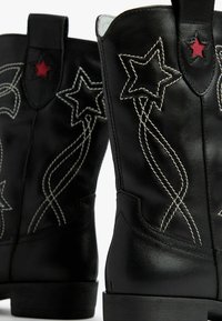 Bottes de cow-boy en cuir noir avec des accents en étoile rouge et des motifs brodés blancs. Bout court et arrondi avec un design de talon bas.