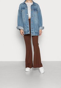 Veste en denim bleu clair avec une coupe oversize et des manches retroussées. Pantalons évasés marron, assortis à des baskets blanches pour un look décontracté.