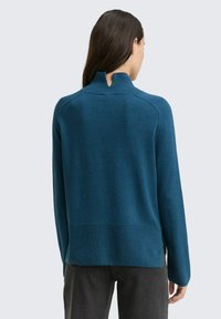 Tiefblaue Sweater mit hohem Kragen und Schlüsselaugen-Detail auf der Rückseite. Hergestellt aus weichem Material, mit geripptem Saum und Bündchen.