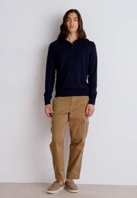 Ναυτικό μακρυμάνικο πουκάμισο πόλο συνδυασμένο με ανοιχτό καφετί cargo παντελόνι, που έχει πλαϊνές τσέπες. Φοριέται με ανοιχτό καφετί παπούτσια χωρίς λουριά.