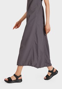 Sandali sportivi neri con cinturini regolabili, soletta imbottita e suola texturizzata, abbinati a un lungo vestito grigio, che evidenzia le calzature.