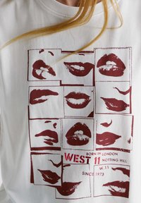 Wit katoenen T-shirt met een herhaald grafisch ontwerp van rode lippen, gecombineerd met de tekst "WEST 11 NOTTING HILL" en "BORN IN LONDON."