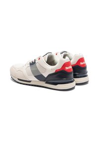 Zapatillas deportivas en beige y azul marino con una parte superior de ante y malla, que presentan un acento rojo en el talón y una suela de goma negra.