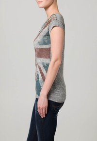 Grå t-shirt med kort ärm som har en Union Jack-design i brunt och blått, med guldfärgad nitar på axeln, figurnära passform, mjuk textur.