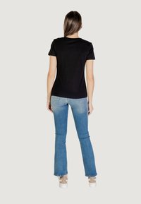 T-shirt nera a maniche corte con scollo rotondo, abbinata a jeans svasati azzurri chiari. Design semplice con una texture liscia.