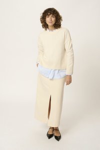 Ljusbeige stickad tröja med ribbat avslut, lagd över en blårandig skjorta. Den krämfärgade kjolen har en slits framtill och är ankle-lång. Svarta spetsiga balettlägenheter fulländar outfiten.