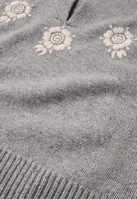 Grau gestrickter Pullover mit gestickten weißen Blumen und kreisförmigen Mustern. Der V-Ausschnitt und das gerippte Saumdetail verleihen Textur.