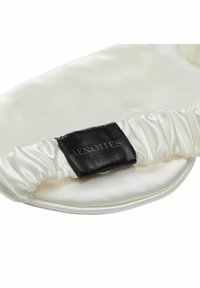 Satin sovmössa i krämfärgad med rynkade kanter, med en svart etikett som säger "Lenoites." Slät textur, rund form.