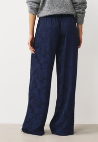 Pantalon large bleu marine avec un motif floral texturé, doté d'une ceinture élastique et d'un tissu doux. Vue de dos.