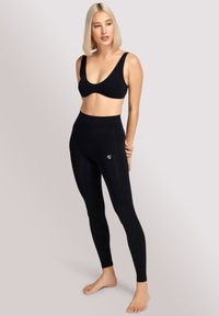 Zwarte sportbeha met brede bandjes en een lage scoop halslijn, gecombineerd met hoge zwarte leggings met een subtiele logo dicht bij de tailleband.