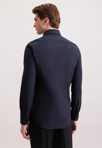 Granatowa koszula z długim rękawem, wykonana z tkaniny teksturowanej, z kołnierzykiem typu spread i guzikami przy mankietach oraz zaokrąglonym dołem.