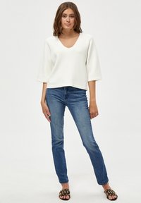 White, V-neck sweater with three-quarter sleeves paired with blue jeans. The sweater has a soft texture and relaxed fit, with casual sandals.